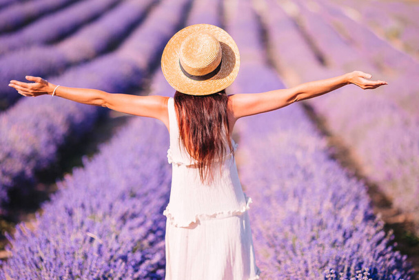 Woman in lavender flowers field at sunset in white dress and hat - Photo, image