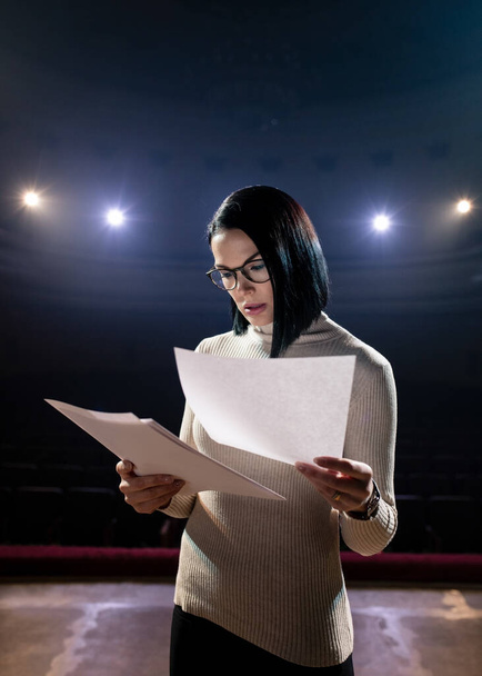 A young girl actress rehearsing her speech on stage. Dark scene with dramatic lighting - 写真・画像