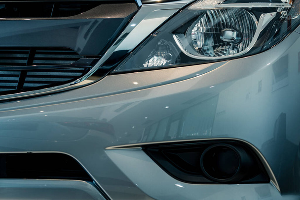 Close-up koplamp van grijze SUV auto geparkeerd in moderne showroom. Glanzende nieuwe auto met reflectie van de moderne showroom. Automobielindustrie. Elektrische auto technologie. Automobiele koplamp. Autodealerconcept - Foto, afbeelding