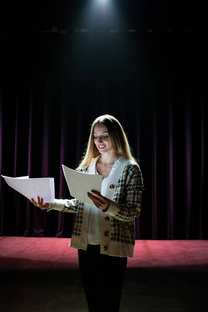 A young girl actress rehearsing her speech on stage. Dark scene with dramatic lighting - Фото, изображение