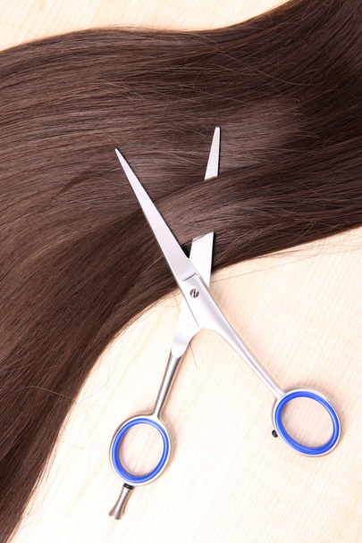 Long brown hair and scissors on wooden background - Photo, image
