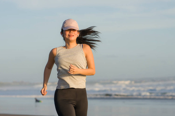 Asian girl running on the beach - young attractive and happy Chinese woman doing jogging workout at beautiful beach enjoying fitness and healthy runner lifestyle - Foto, imagen