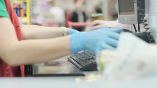 Werknemer bij de kassa in de supermarkt controleren producten in rubberen handschoenen op een commodity tape. Coronavirus infectie bescherming. Voorbereiding voor quarantaine. - Video