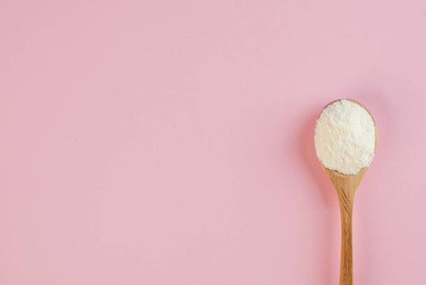  White collagen powder on a wooden spoon on a pink background. Skin care, rejuvenation. Copy space. High quality photo - Foto, Imagem
