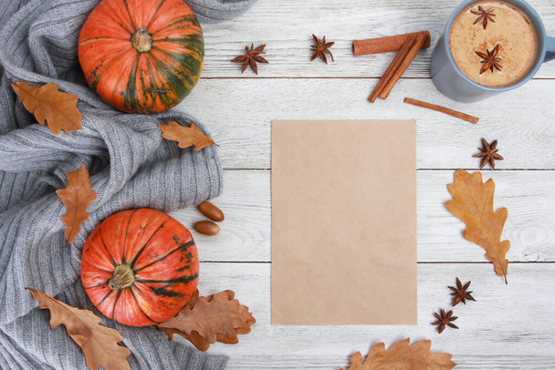 Spicy coffee with milk, grey plaid, spices, dry oak leaves, acorns, orange pumpkins, blank craft paper on white wooden table. Autumn drink concept. Fall, pumpkin latte, thanksgiving, top, copy space - 写真・画像
