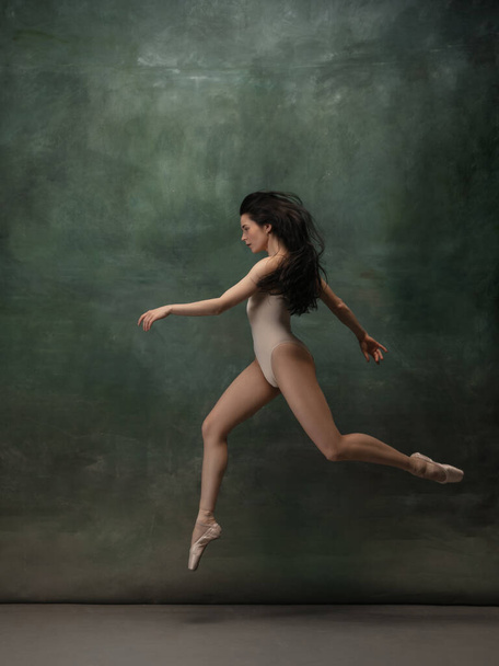 Young graceful tender ballerina on dark green studio background - Foto, imagen