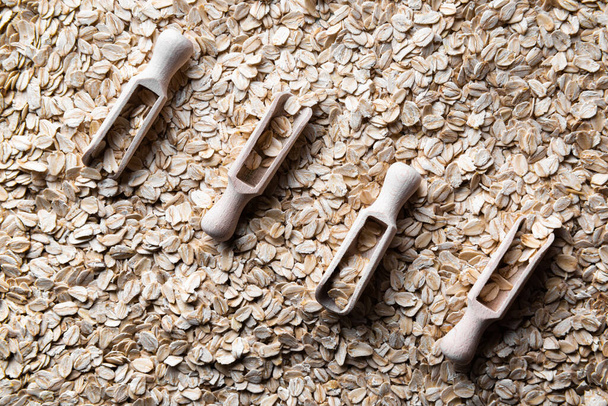 Diagonal of four wooden scoops with flakes of rolled oats in them. Scoops are on layer of rolled oats. Source of vegetable protein. Healthy and sport eating concept background. Horizontal orientation. - Photo, Image