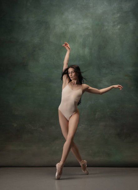 Young graceful tender ballerina on dark green studio background - 写真・画像