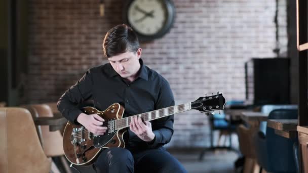 handsome man in black shirt playing on guitar beautiful blues composition in cafe. Retro studio, brick interior. Jazz, Blues, Funk. Medium long shot - Кадри, відео