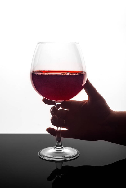 Une main de femme tient un verre de vin rouge sur un fond noir et blanc. - Photo, image