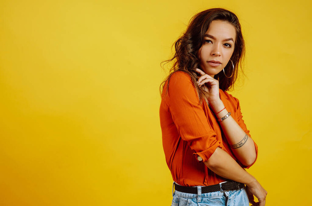 Portrait of young girl posing on yellow background. Pretty woman  wears a carrot blouse and jeans. Fashion and lifestyle concept. - Fotoğraf, Görsel