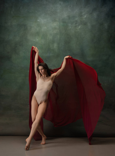 Young graceful tender ballerina on dark green studio background - Fotó, kép