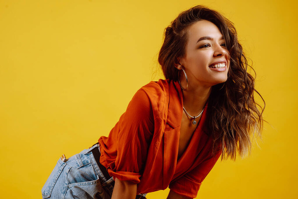 Portrait of young girl posing on yellow background. Pretty woman  wears a carrot blouse and jeans. Fashion and lifestyle concept. - Zdjęcie, obraz