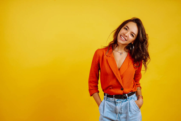 Portrait of young girl posing on yellow background. Pretty woman  wears a carrot blouse and jeans. Fashion and lifestyle concept. - Foto, afbeelding