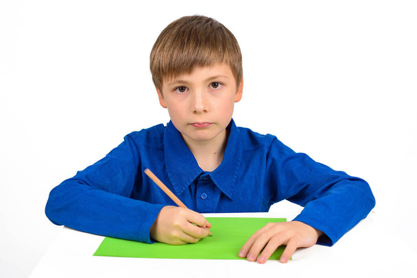 desarrollo infantil: un colegial con una camiseta azul se sienta a la mesa y dibuja sobre papel de colores - Foto, imagen
