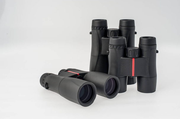 Tres prismáticos de diferentes tamaños con detalles rojos sobre fondo blanco
 - Foto, Imagen
