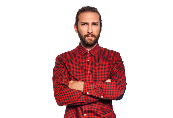 Serious young man in red plaid shirt with beard with crossed arms gazing intently at the camera isolated on white background - Valokuva, kuva