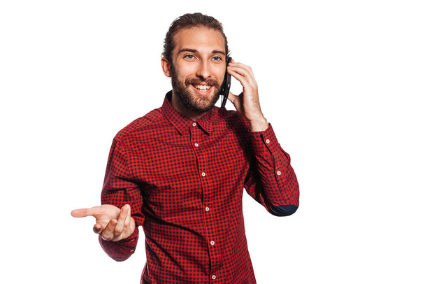 Happy young man in red plaid shirt with beard smiling and talking on cell phone isolated on white background - Фото, изображение