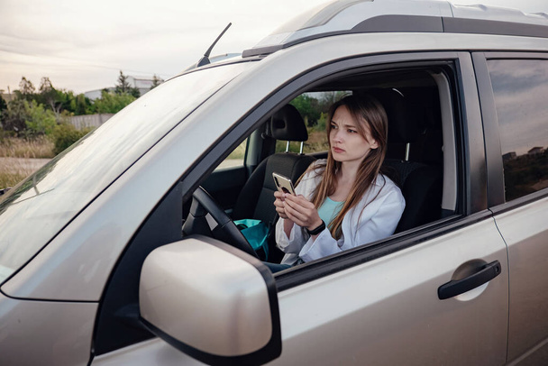 egy gyönyörű fiatal nő szürke autót vezet. egy nő GPS-t használ a mobiltelefonján. az autóutazás, a hajózás és a szabadság gondolata és koncepciója - Fotó, kép