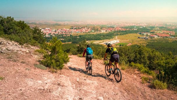 Twee fietsers vrienden met helmen en rugzakken rijden mountainbikes in de berg. Hoge hoek uitzicht op Eskisehir stadsgezicht. - Foto, afbeelding