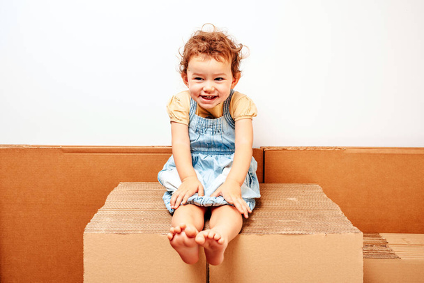 Porträt eines Mädchens, das auf einem Kartonstapel sitzt - Foto, Bild