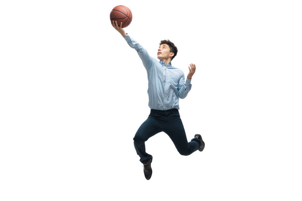 Muž v kancelářských šatech hraje basketbal na bílém pozadí. Neobvyklý pohled obchodníka v pohybu, akce. Sport, zdravý životní styl. - Fotografie, Obrázek