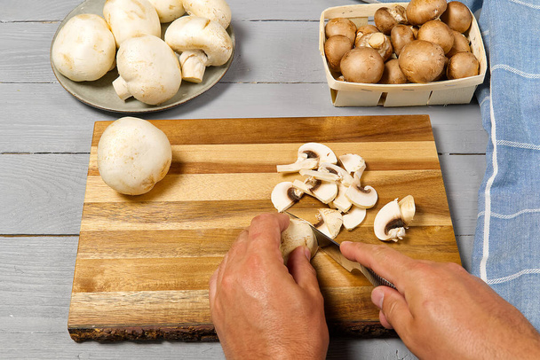 Man handen snijden verse champignon champignons. Witte en bruine champignon op grijze houten tafel gesneden champignons. - Foto, afbeelding