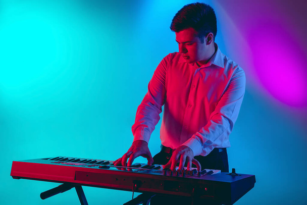 Young caucasian musician, keyboardist playing on gradient background in neon light. Concept of music, hobby, festival - Foto, Imagen