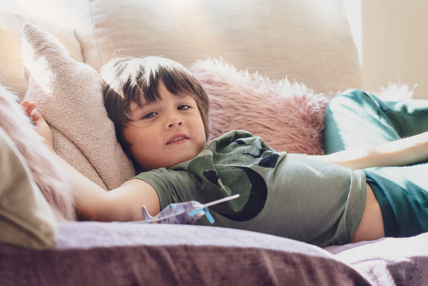 Korkea avain valo onnellinen poika makaa pörröinen tyyny sohvalla, valikoiva keskittyä Suloinen lapsi hymyilevät kasvot rentouttava kotona viikonloppuna, Lämmin ja viihtyisä kohtaus Pastel tone - Valokuva, kuva