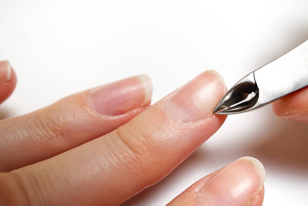 Womans hand removing nail cuticle on light white table. Care about dry, overgrown cuticle. Closeup. - Фото, зображення