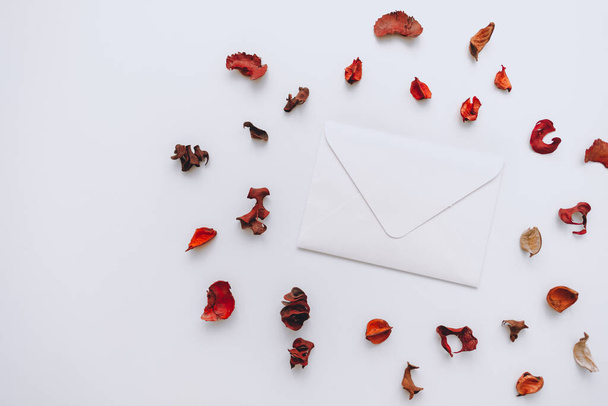 White blank paper envelope on a white background around decorated with dried petals. Copy space. High quality photo - Photo, Image
