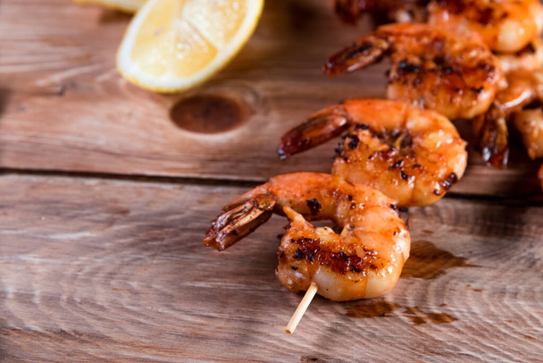 Appetizing fried shrimp on a skewer on a wooden surface among lemon and seasonings. The concept of fast and wholesome food - Valokuva, kuva