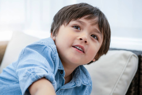 Porträt eines glücklichen kleinen Jungen, der mit lächelndem Gesicht nach oben blickt, gesundes Kind, das sich zu Hause entspannt, Kindergesicht mit Lächeln in Großaufnahme. Positives Kinderkonzept - Foto, Bild