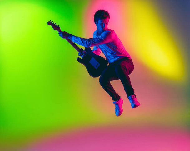 Young caucasian musician, guitarist playing on gradient background in neon light. Concept of music, hobby, festival - Фото, зображення