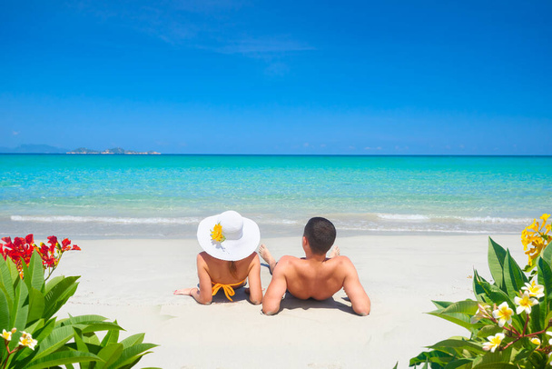 Mladý pár odpočívá na tropické pláži v létě slunečný den na pozadí jasné modré oblohy a tyrkysové moře. - Fotografie, Obrázek