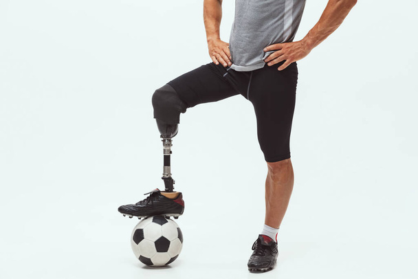 Athlete with disabilities or amputee isolated on white studio background. Professional male football player with leg prosthesis training and practicing in studio. - Fotó, kép