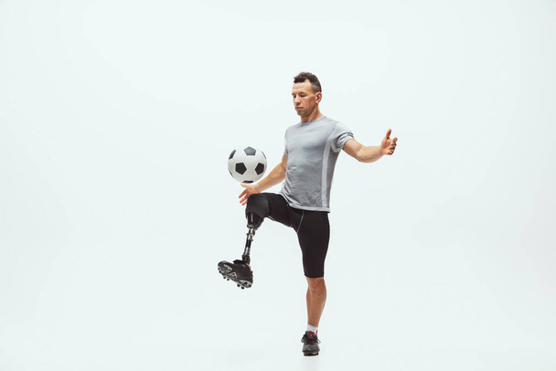 Athlete with disabilities or amputee isolated on white studio background. Professional male football player with leg prosthesis training and practicing in studio. - Zdjęcie, obraz