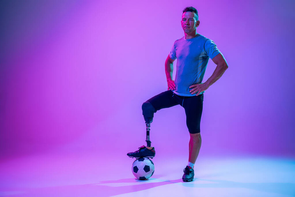 Athlete with disabilities or amputee isolated on gradient studio background. Professional male football player with leg prosthesis training and practicing in studio. - 写真・画像