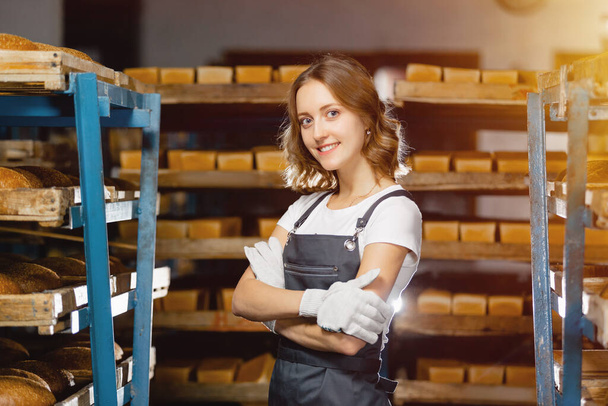 Portrait of a baker girl against the background of shelves with fresh bread in a bakery. Industrial bread production - Foto, Bild