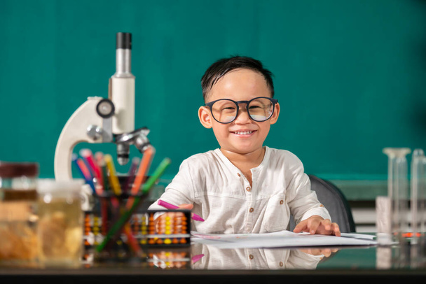 Маленький азіатський хлопчик робить домашнє завдання. Розумний малюк за столом. школяр. Початкова школа малювання на робочому місці. Хлопцю подобається вчитися. Домашня освіта. Знову в школу. Маленький хлопчик на уроці - Фото, зображення