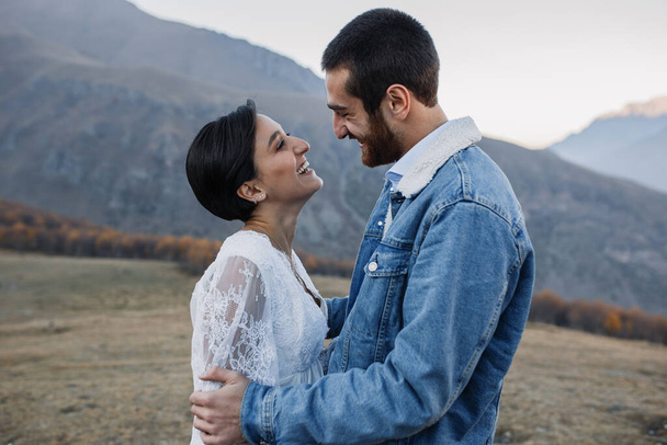 Νεαρό ζευγάρι Γεωργιανών ποζάρουν στα βουνά. Γάμος Boho στη Γεωργία. Βραδινό ηλιοβασίλεμα. Μπλε τζιν μπουφάν - Φωτογραφία, εικόνα