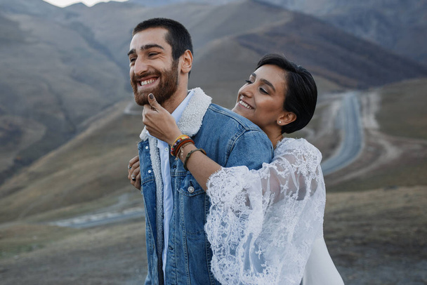 Giovane coppia georgiana in posa sulle montagne. Matrimonio Boho in Georgia. Sera al tramonto. Giacca blu jeans - Foto, immagini