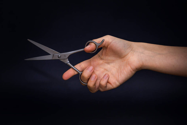 Передняя фотография руки, держащей металлические ножницы, расположенные на черном фоне, с мягкой текстурой.  - Фото, изображение