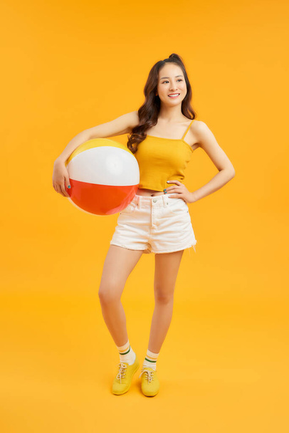 gelukkig jong aziatisch vrouw holding strand bal in de zomer vakantie reizen op oranje achtergrond. - Foto, afbeelding