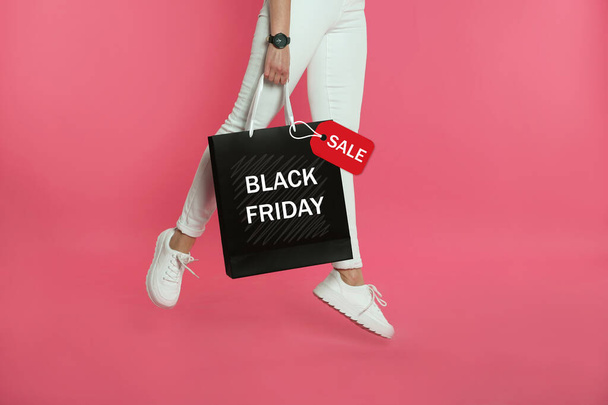 Woman jumping with shopping bag on pink background, closeup. Black Friday Sale - Photo, Image