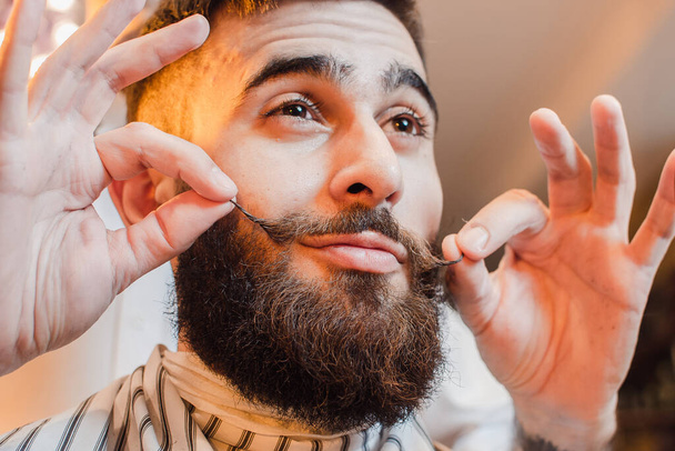 Barber makes a styling mustache for a young handsome guy in a male barber shop. Barber Shop. - Photo, Image