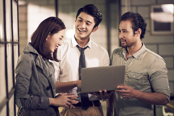 un team di tre giovani imprenditori asiatici che hanno una discussione utilizzando il computer portatile in ufficio felice e sorridente - Foto, immagini