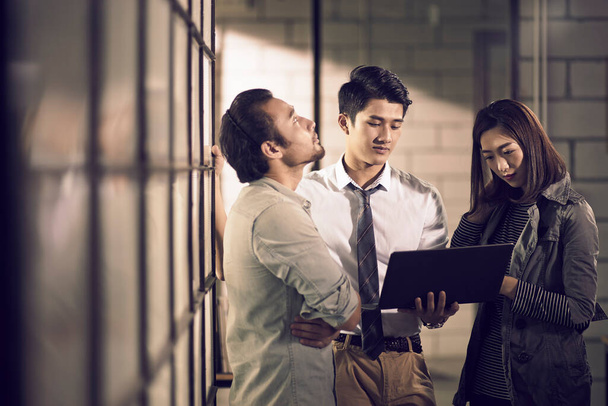 команда из трех молодых азиатских предпринимателей, встречающихся в офисе, обсуждающих использование ноутбука в офисе - Фото, изображение
