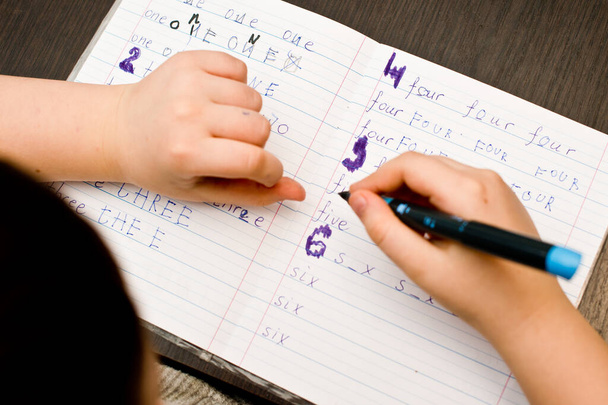 Το παιδί διαβάζει. Εργασία στο σχολείο, άσκηση γραφής στο χέρι. Μαθαίνω να γράφω ονόματα αριθμών.. - Φωτογραφία, εικόνα