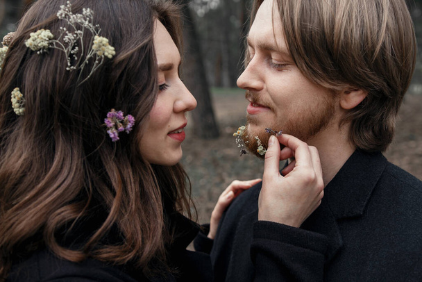 Jeune couple dans la forêt. Histoire d'amour, manteau noir et fleurs séchées. - Photo, image
